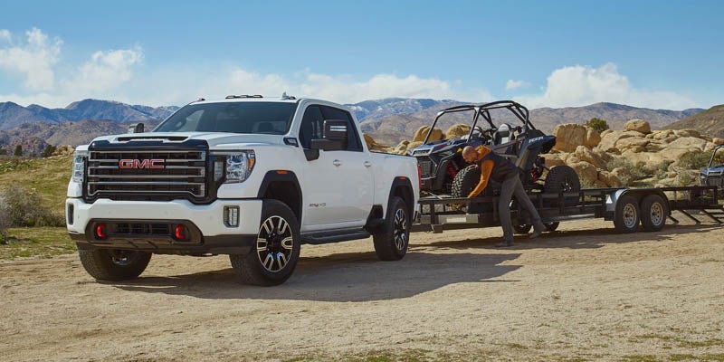 GMC Sierra 2500HD pickup truck towing a large black trailer on a sandy area.